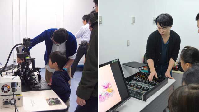 手作り蛍光顕微鏡について説明する研究員とスーパーコンピューターの基板の説明をする研究員